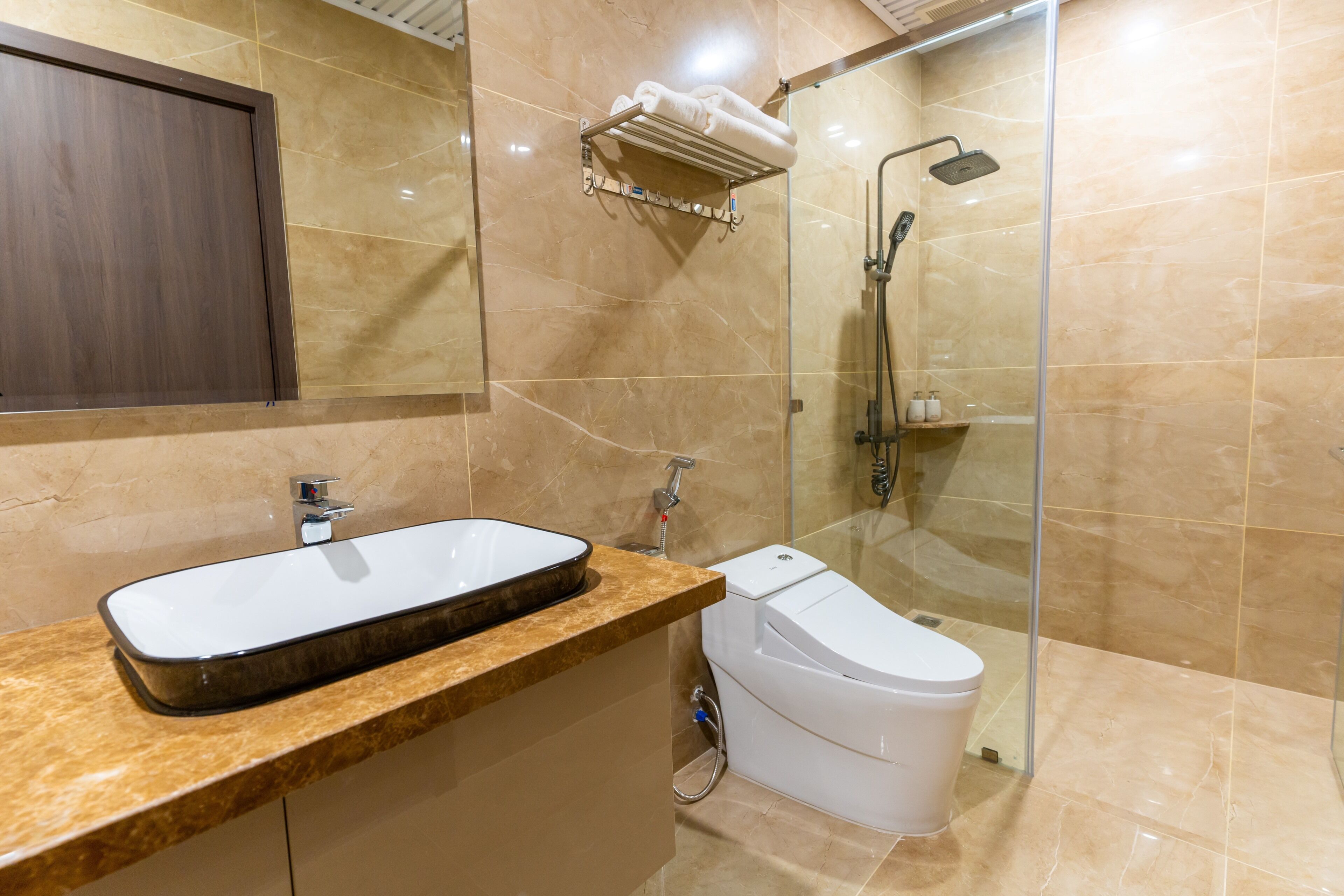 A bathroom with a marble vanity, a toilet, a glass shower enclosure, and a towel rack with towels.