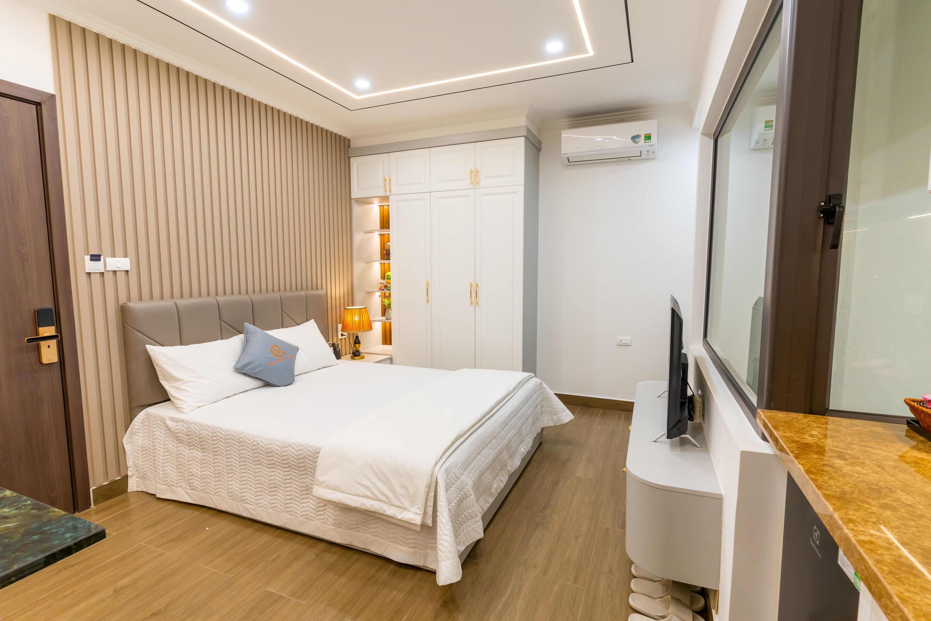 A modern hotel room with a large bed, a TV, a wardrobe, and a desk.