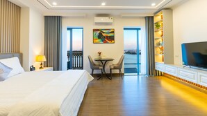 A hotel room with a bed, a desk with two chairs, a television, and a view of the city. - CM Hotel & Apartment (Hai Phong)