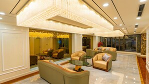 A spacious lobby with plush seating, a grand chandelier, and a reflective glass wall. - CM Hotel & Apartment (Hai Phong)