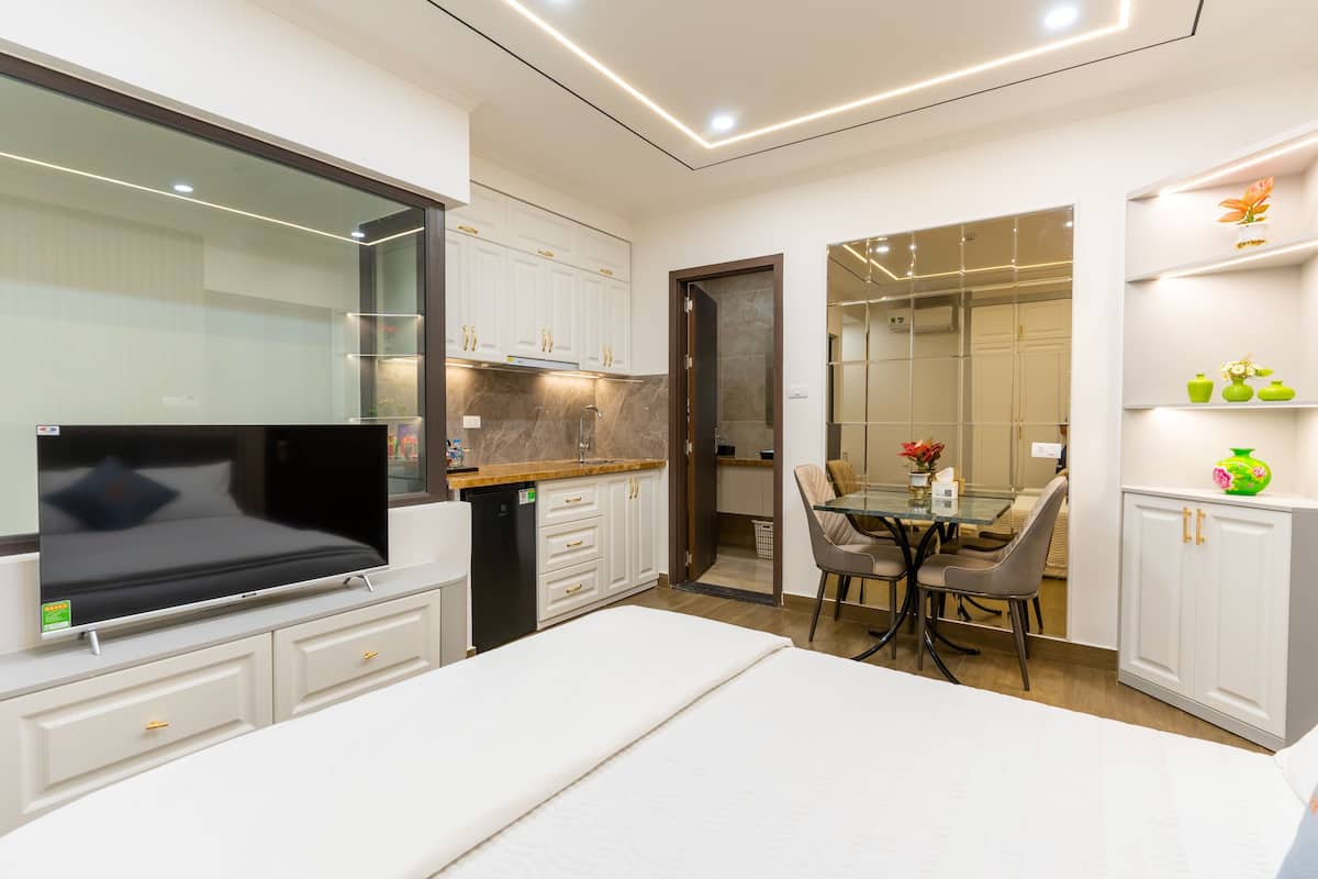 A modern kitchen with white cabinets, a dining area with a glass table, and a TV mounted on the wall.