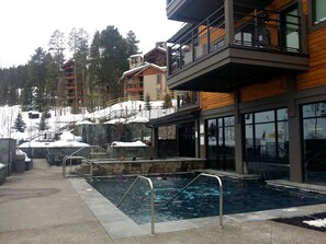 Ein Poolbereich mit Holzterrasse, Pool und einem Gebäude mit Balkonen und großen Fenstern.