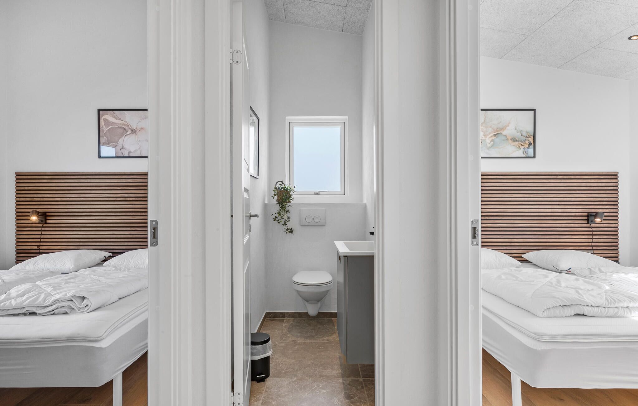 A modern hotel room with two beds, a small bathroom, and a view through an open door.