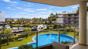 Un balcon avec vue sur une piscine, des palmiers et le paysage urbain.