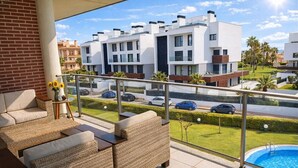Un balcon agrémenté de meubles en osier, une piscine et, au loin, des bâtiments modernes.
