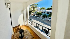 Een balkon met een houten tafel, een lantaarn en uitzicht op een straat met auto's en gebouwen.