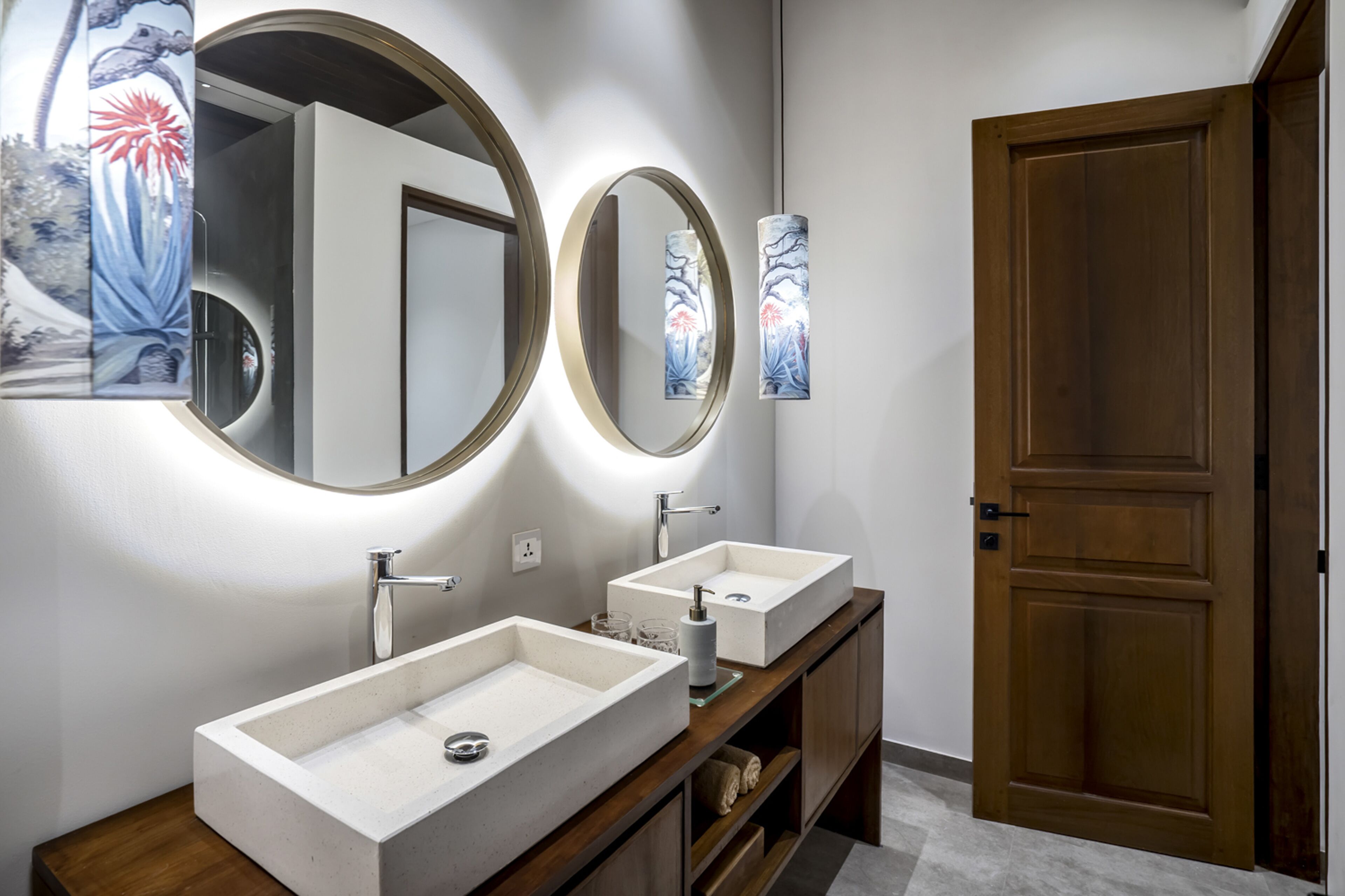 Un baño moderno con dos lavamanos blancos rectangulares, un mueble de tocador de madera y una puerta de madera.