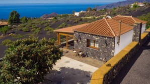 Ein Küstenanwesen mit einem Steinhaus, einem Ziegeldach, einer Terrasse mit Sitzgelegenheiten und Blick auf Meer und Hügel.