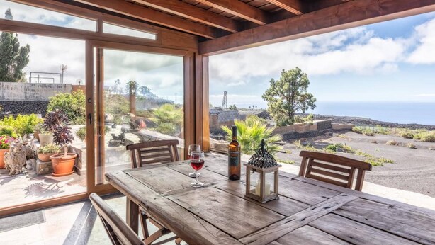 Ein Holztisch mit einer Flasche und einem Glas, platziert in einem Raum mit großen Fenstern, die eine schöne Landschaft zeigen.