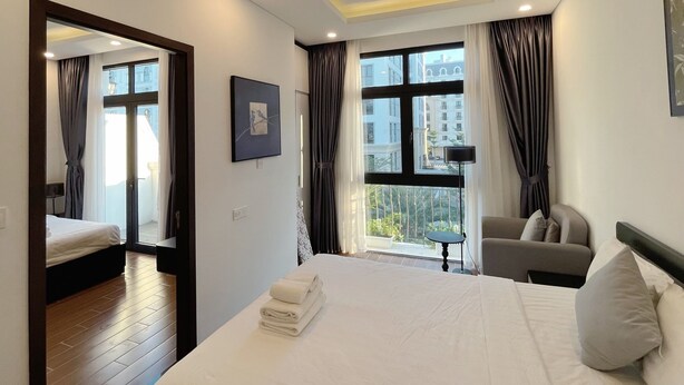 A hotel room with a bed, a desk, a chair, and a window with curtains. - Le Palmier Phu Quoc Hotel (Phu Quoc)