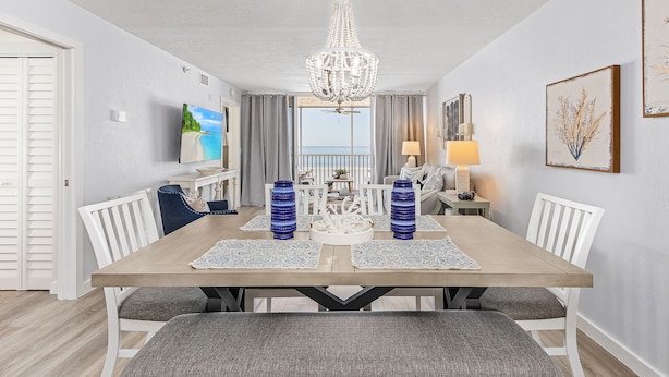 A dining area with a wooden table, white chairs, blue vases, and a chandelier.