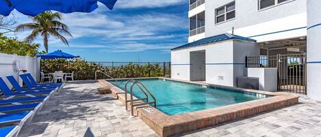 Un área de piscina con sillones de descanso, piscina y un edificio con balcones.