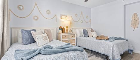 A bedroom with two beds, a ceiling fan, wall decorations, and a bedside table with a lamp.