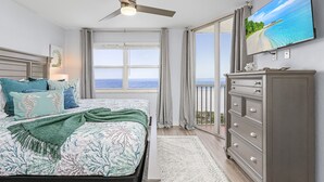 A bedroom with a bed, a dresser, a television, and a view of the ocean.