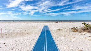 A beach with a blue running track leading to the water, people sunbathing, and a clear sky.