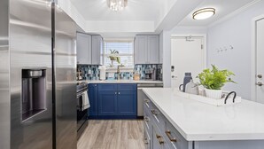 A modern kitchen with stainless steel appliances, blue cabinets, and a white countertop.