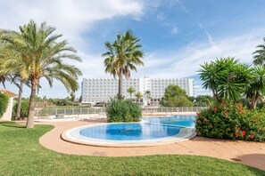 A swimming pool surrounded by palm trees and a hotel building in the background.