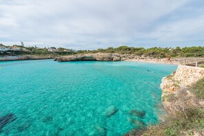 A coastal area with clear turquoise water, rocky formations, and a beach with people. - ES MIRADOR (CALES DE MALLORCA) - Fantastic flat with shared pool near the sea - free WiFi (Manacor)