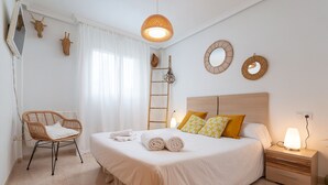 Et pænt opredt soveværelse med seng, sengebord, lampe, stol og dekorative ting på væggen.