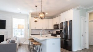 Una cocina moderna con armarios blancos, electrodomésticos de acero inoxidable y una isla central con taburetes.