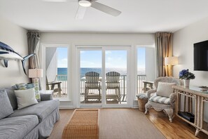 A spacious living room with a large sliding glass door leading to a balcony with outdoor seating. - Gulf-front Condo • Shared Pool + Private Balcony + Beach Access | Blue Marlin (Panama City Beach)