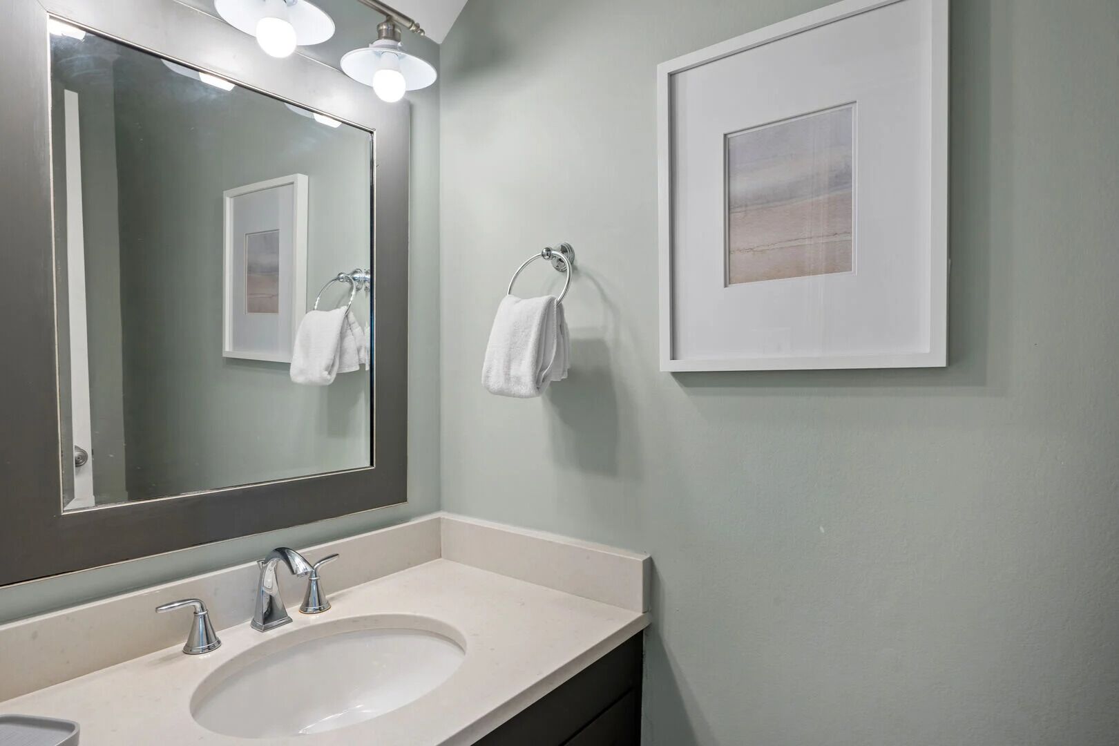 A bathroom with a large mirror, a sink, and a towel rack.