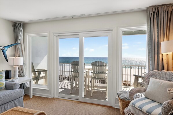 Una habitación con vistas a la playa, un sofá blanco, una silla de mimbre y una mesa con lámpara.