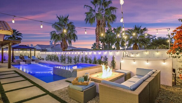 Un jardin avec une piscine, un espace salon extérieur et des guirlandes lumineuses.