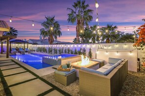 Un jardin avec une piscine, un espace salon extérieur et des guirlandes lumineuses.