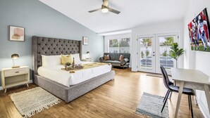 Une chambre dotée d’un grand lit, d’un ventilateur de plafond, d’une table de chevet et d’une commode, et offrant une vue sur l’extérieur grâce à une porte-fenêtre coulissante.