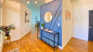 Un couloir doté d’un plancher en bois, d’un mur d’accent bleu, d’un miroir rond et d’une console sur laquelle sont posés un bol et une plante.