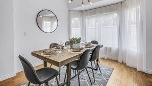 Un coin repas avec une table en bois dressée pour quatre personnes, des chaises noires, un miroir rond et un lustre moderne.