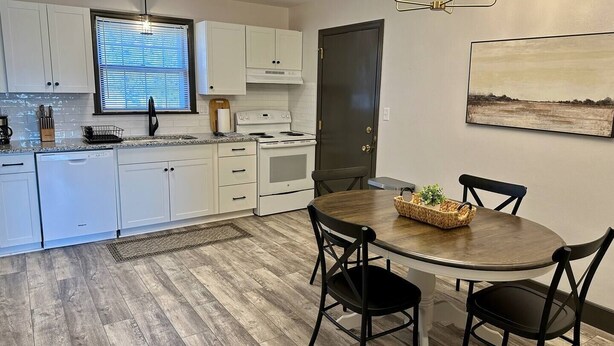 Una cocina moderna con armarios blancos, horno empotrado y comedor con mesa de madera y sillas negras.