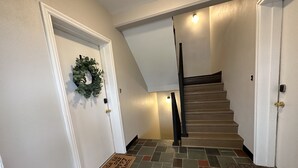 Una escalera con barandilla, un felpudo y una puerta decorada con un adorno navideño.
