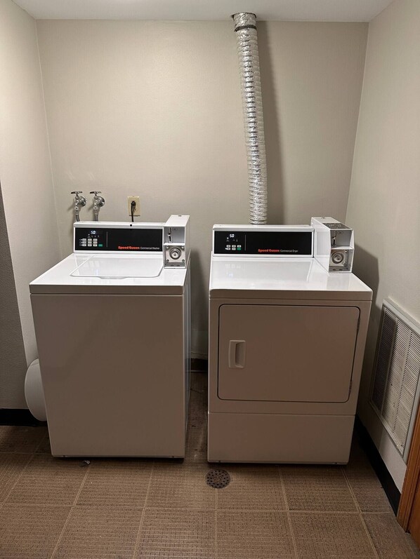 Twee witte wasmachines met voorlader, digitale displays, een ventilatiepijp en een geventileerde airconditioningunit.