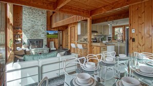 A cozy cabin interior with a stone fireplace, wooden walls, a dining area with white chairs, and a kitchen with wooden cabinets. - 3 Br: N Westridge 222-7 Alpenglow: 3BR,2 Bath (Snowshoe)