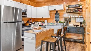 A kitchen with white cabinets, a stainless steel refrigerator, a coffee bar, and a wooden ceiling.