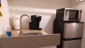 Eine Küchenzeile mit einem Edelstahlkühlschrank, einer Mikrowelle, einer Kaffeemaschine und einem Papiertuchspender.