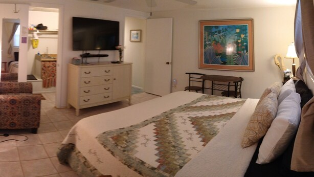 Ein Schlafzimmer mit einem Bett, einem Schminktisch, einem Fernseher, einem Gemälde und einem Sessel.