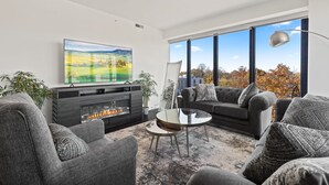 A modern living room with a fireplace, grey sofas, a coffee table, and a large TV. - "Faith of Evanston" 180°view, 2BDR +2Bath Urban luxury (Evanston)