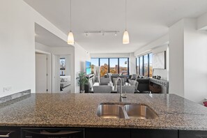 Une cuisine moderne dotée de plans de travail en granit, d’un évier double et de luminaires suspendus.