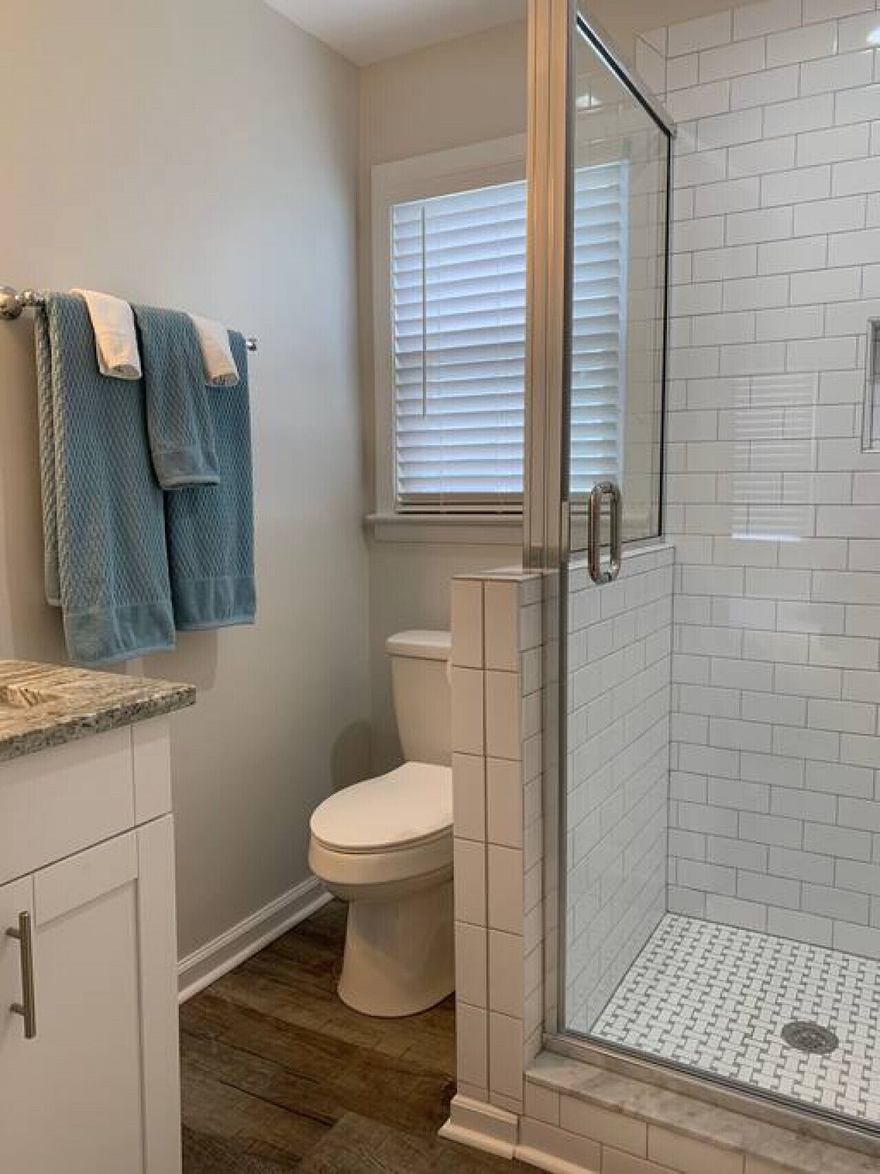 A bathroom with a toilet, a glass-enclosed shower, and a window with blinds.