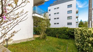 Un edifici modern d'apartaments amb balcons, un jardí ben cuidat i un cel blau clar.