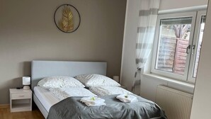 A modern bedroom with a bed, bedside table, and a window with curtains. - Gartenparadies Apartment  in Urbar (Urbar)
