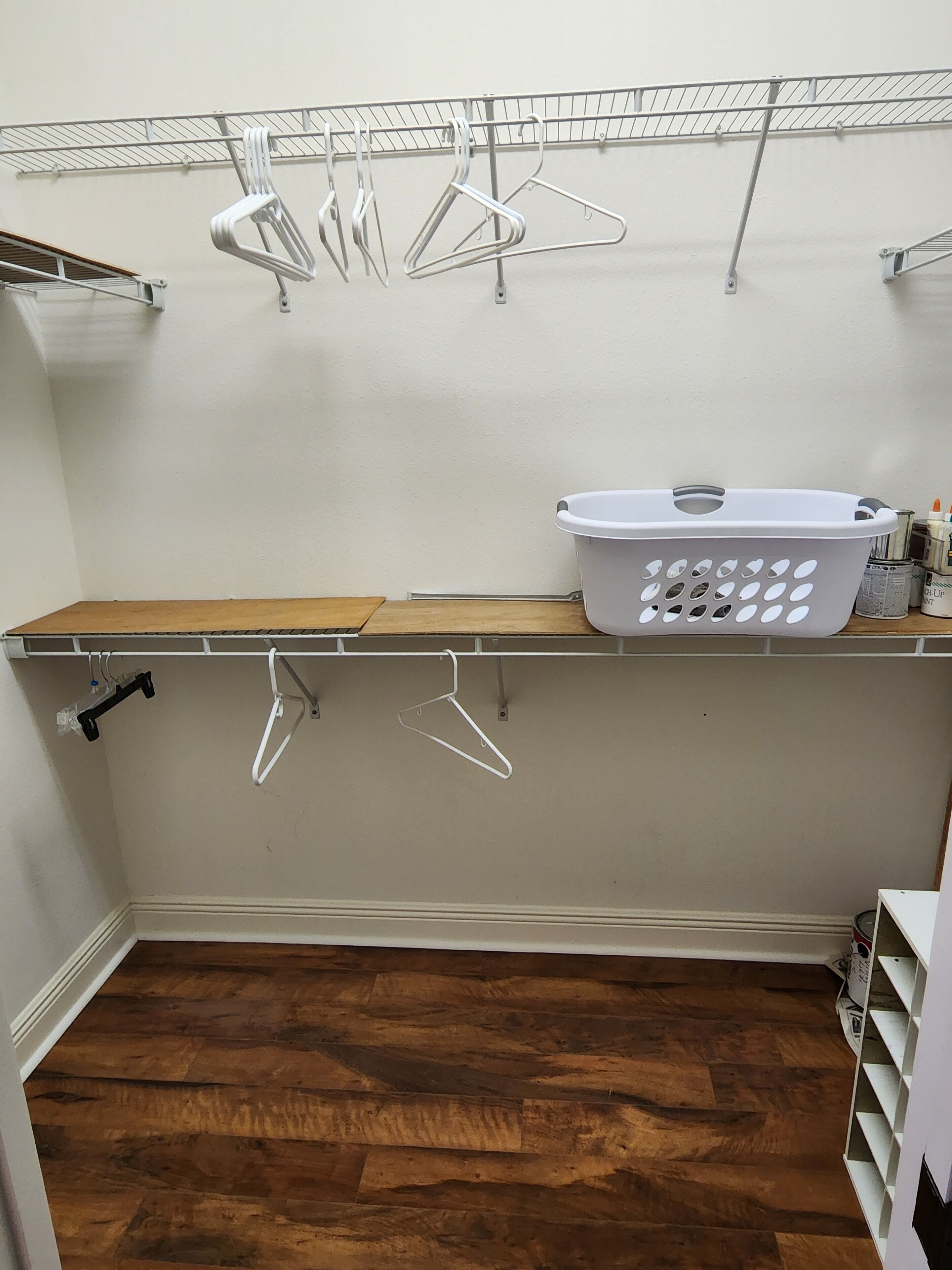 A laundry room with a wooden shelf, a white laundry basket, and metal hangers on a rack.