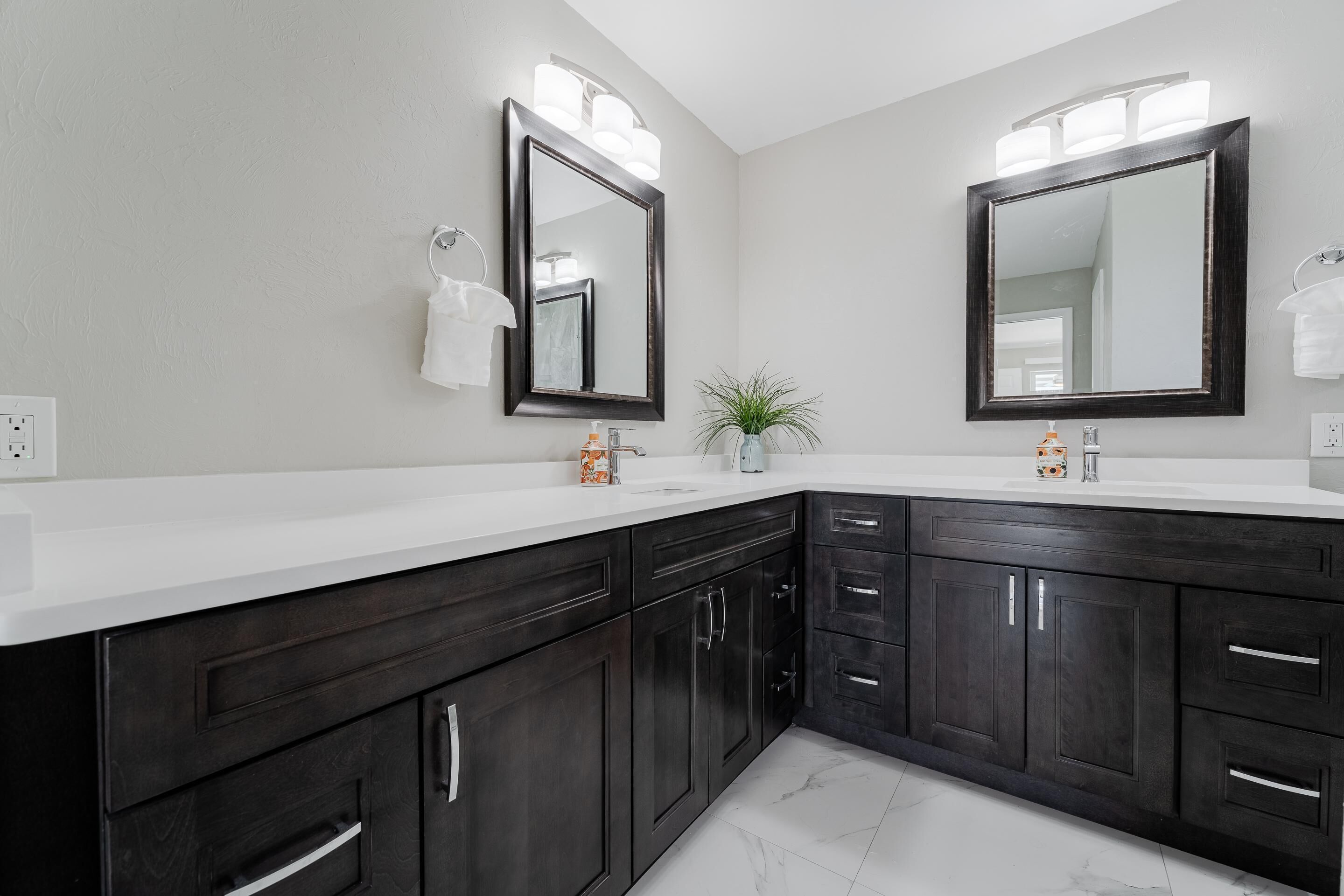 A modern bathroom with dark wood cabinets, white countertops, and dual vanity mirrors with light fixtures.