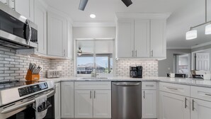 A modern kitchen with white cabinets, a stainless steel dishwasher, and a brick backsplash.