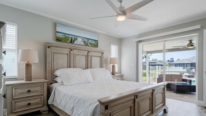 A bedroom with a large bed, two bedside tables, a ceiling fan, and a view of the outdoors.