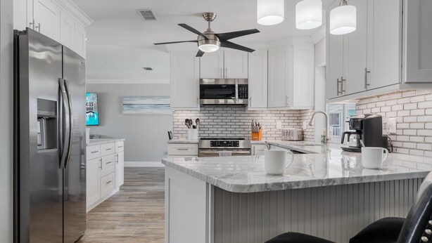 A modern kitchen with white cabinets, a stainless steel refrigerator, a central island with a sink, and a ceiling fan.