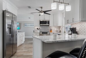 A modern kitchen with white cabinets, a stainless steel refrigerator, a central island with a sink, and a ceiling fan. - Gulf Access, Kayaks, Bikes, Ping-Pong & Pool - Villa Palaco Palazzo - Roelens Vacations (Cape Coral)